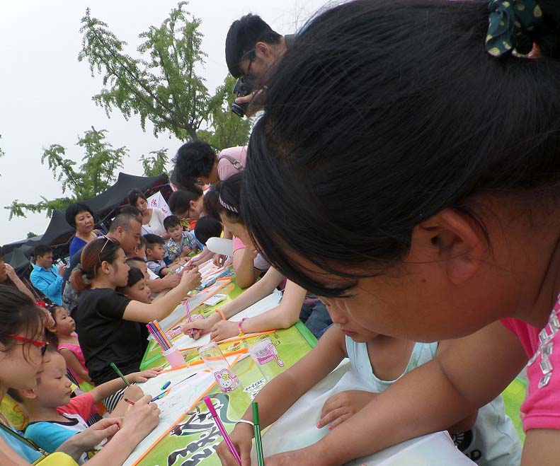 濱江公園小朋友及家長正在風(fēng)箏上繪畫，并寫下自己的環(huán)保寄語。